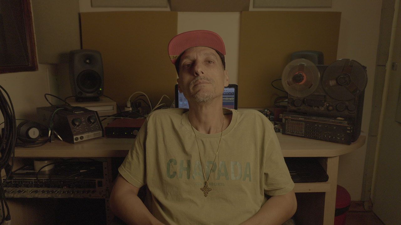 Gabriel Jahbê no estúdio com camiseta Chapada, cercado por equipamentos e luz quente